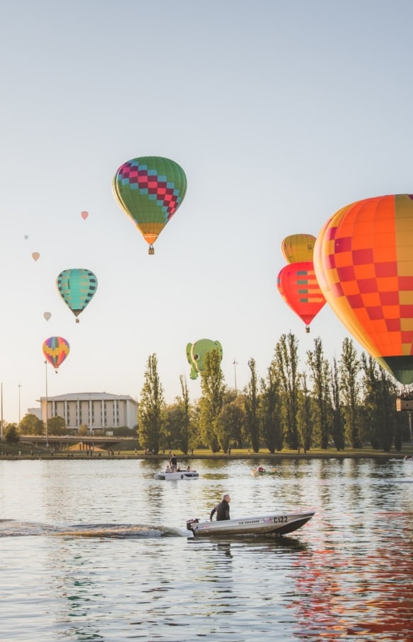 Balon udara melayang di atas perairan tenang Lake Burley Griffin yang dilayari perahu di Canberra, Australian Capital Territory © EventsACT