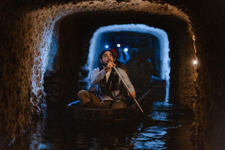 Un uomo con una luce da testa che pagaia su una piccola imbarcazione tra antichi tunnel durante il Fremantle Prison Tunnels Tour, Fremantle, Western Australia