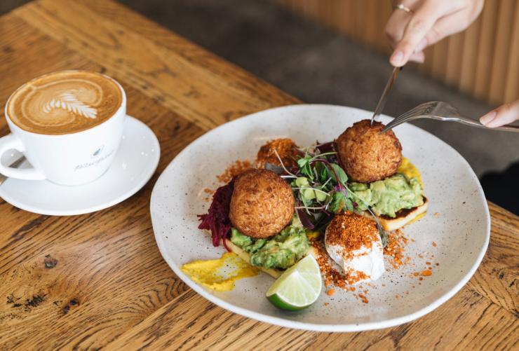 Una persona che taglia un bocconcino di formaggio fritto gourmet su un toast di avocado con un caffè di lato al Pawpaw Cafe, Brisbane, Queensland © Pawpaw Cafe