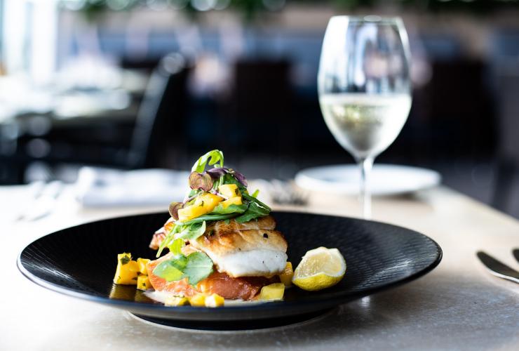 Un piatto a base di barramundi con limone accanto a un bicchiere di vino bianco al Dundee’s Waterfront Restaurant, Cairns, Queensland © Alexandra Gow