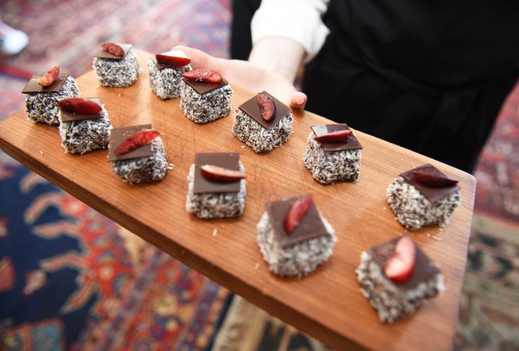 Una persona con un vassoio di lamington ricoperti di cioccolato e frutta al The Great Aussie Brunch, World's 50 Best Restaurants © Tourism Australia